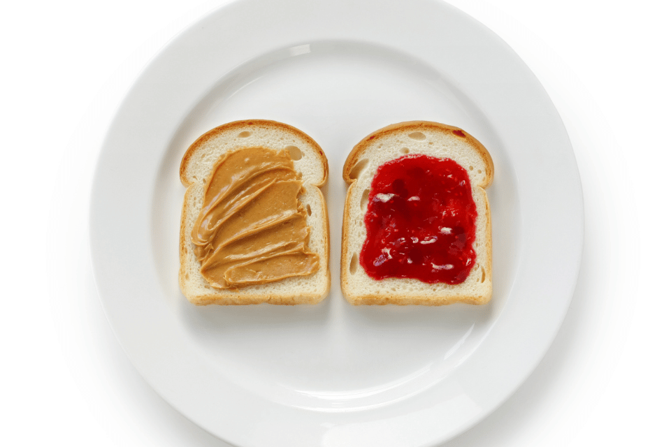Two slices on white bread, one has peanut butter and the other has jelly.