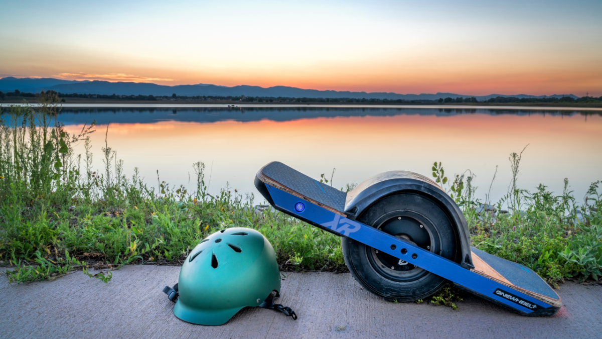 A Onewheel sits on the sidewalk next to a lake at sunset.